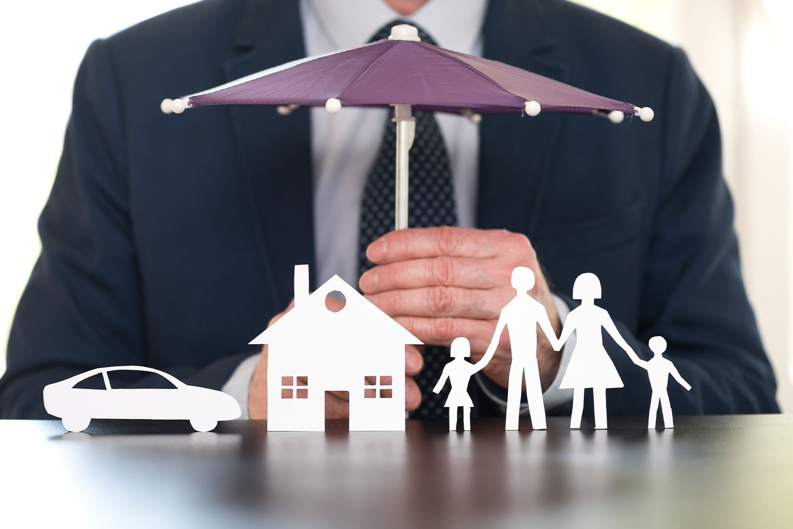 Image of man holding small umbrella over paper cut out a house, care, and family